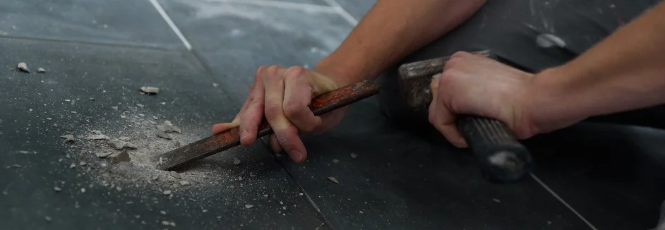 Person entfernt Fliese mit Meißel